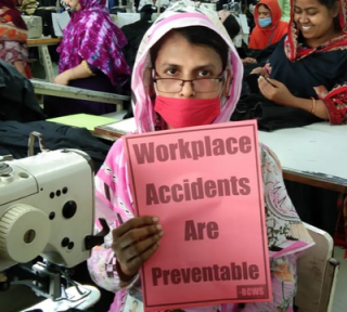 Trabajadora de la confección sosteniendo cartel "Los accidentes laborales pueden prevenirse"